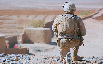 Soldier in the field crouching down looking out over a desert town